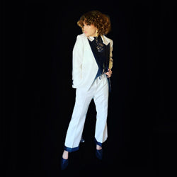 Person wearing a white tailored suit with black shirt and accessories from Addicted Bespoken posing confidently against a black background