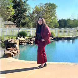 Woman wearing a burgundy tailored suit from Addicted Bespoken posing outdoors by a swimming pool with trees and a white fence in the background