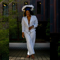 Woman wearing a white tailored suit from Addicted Bespoken with a decorated graduation cap, walking outdoors and smiling