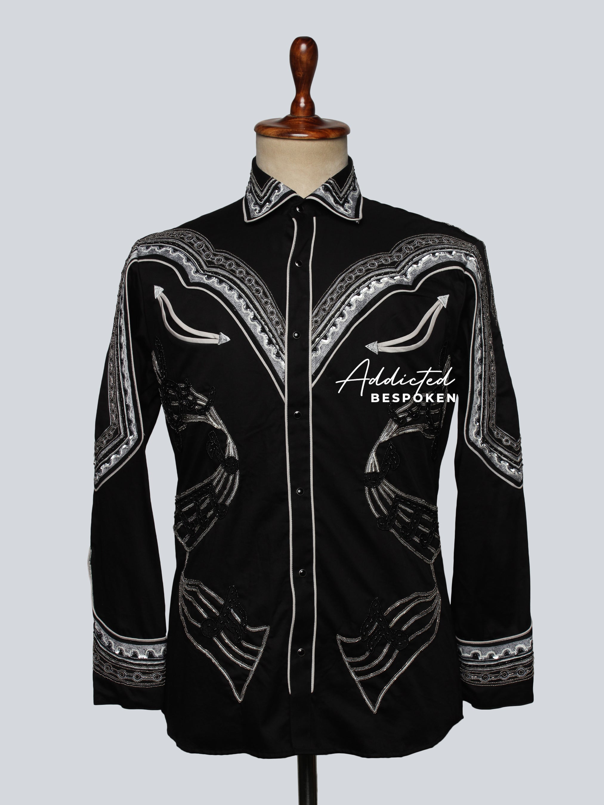 A black long-sleeved men's shirt with white embroidered geometric patterns and a collar, displayed on a mannequin.