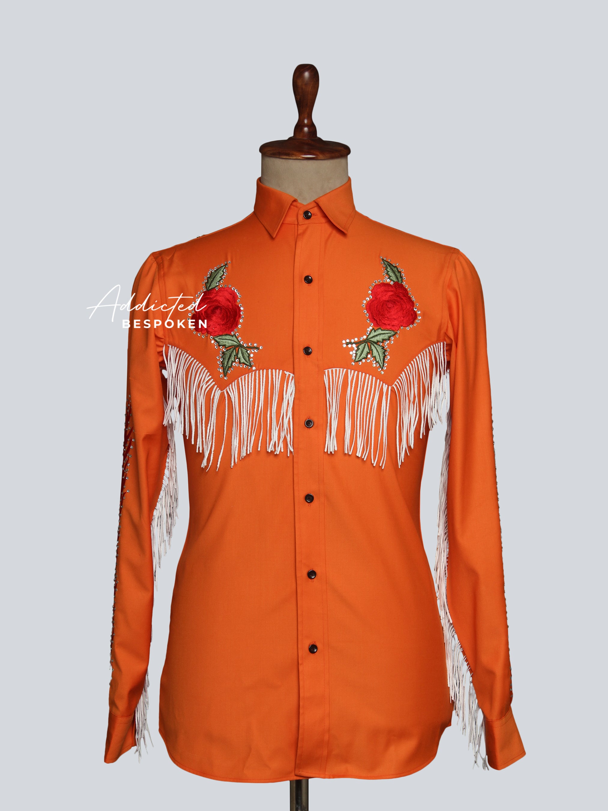 An orange men's shirt with intricate embroidery and fringes displayed on a mannequin.