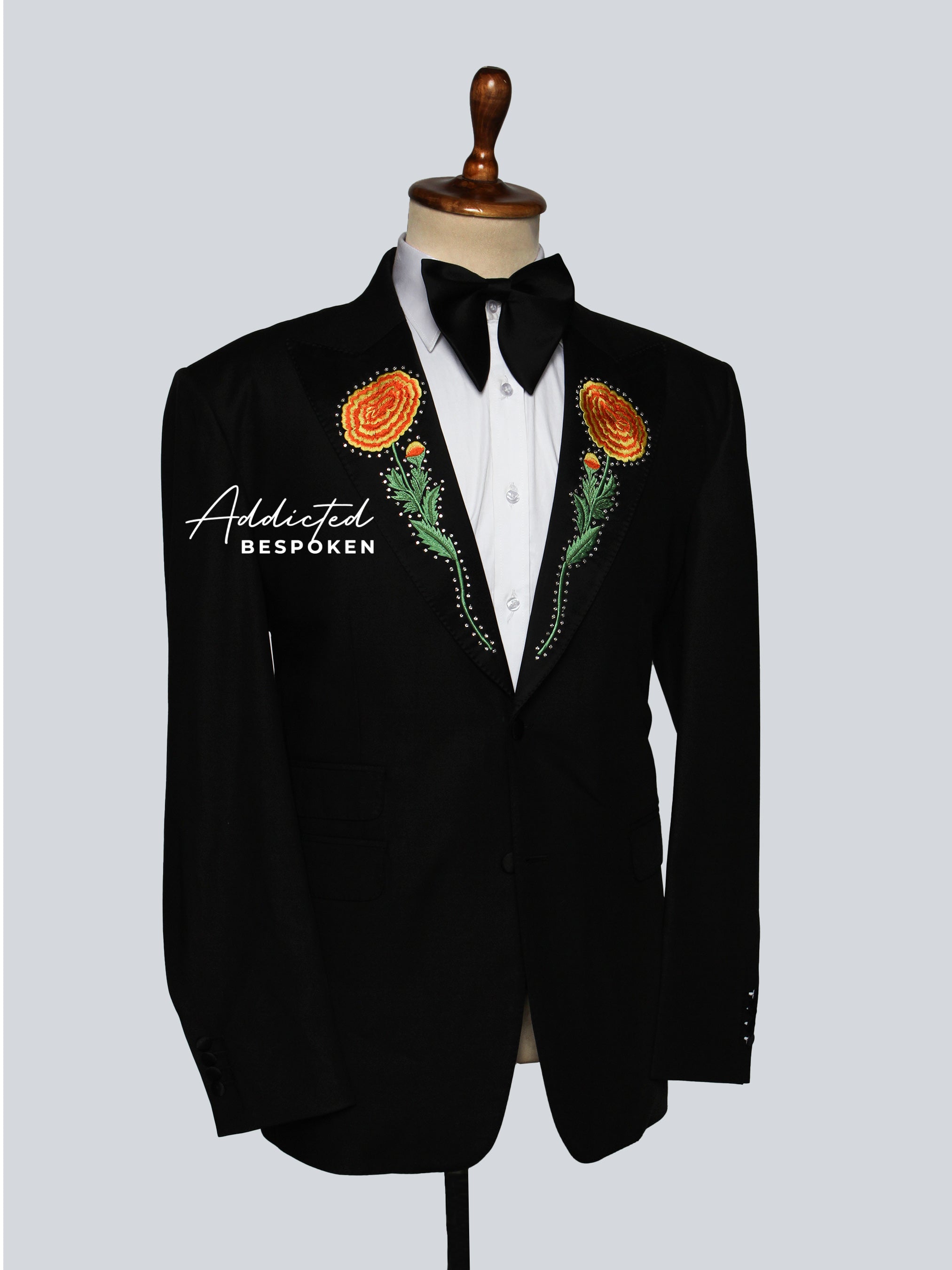 Side View of a Black tuxedo jacket with floral boutonnieres on a mannequin against a light gray background.