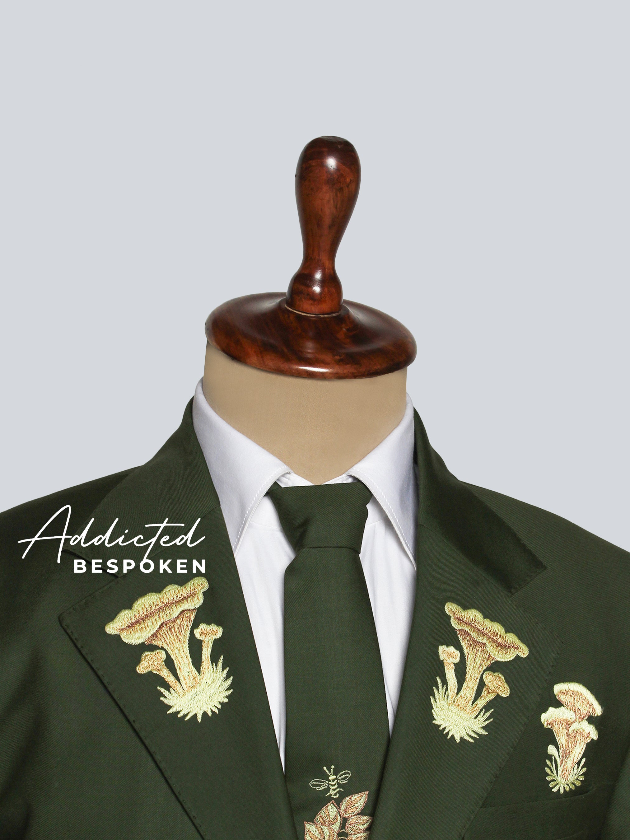 Green suit jacket with floral embroidery on a mannequin against a gray background, featuring the brand 'Addicted Bespoken'.