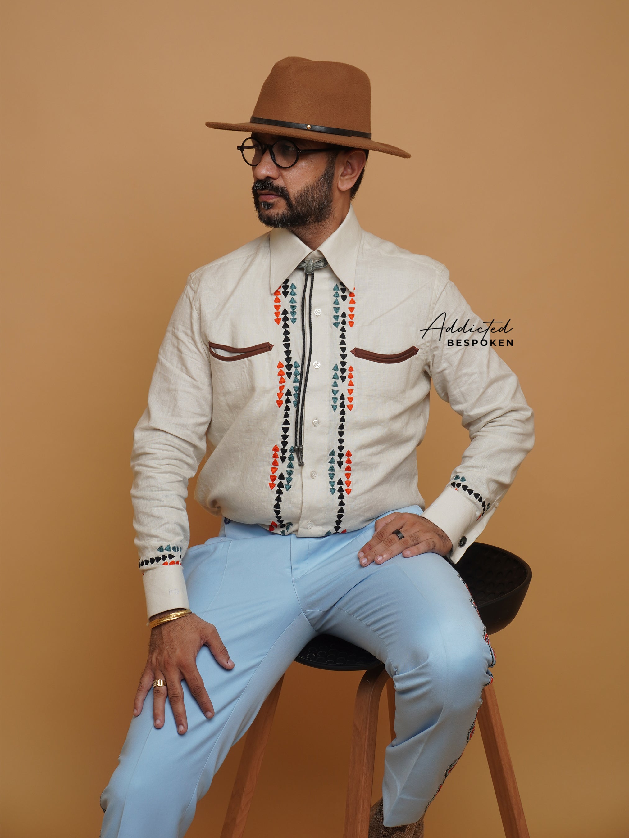 Seated view of male model wearing cream embroidered western shirt with hat β Addicted Bespoken