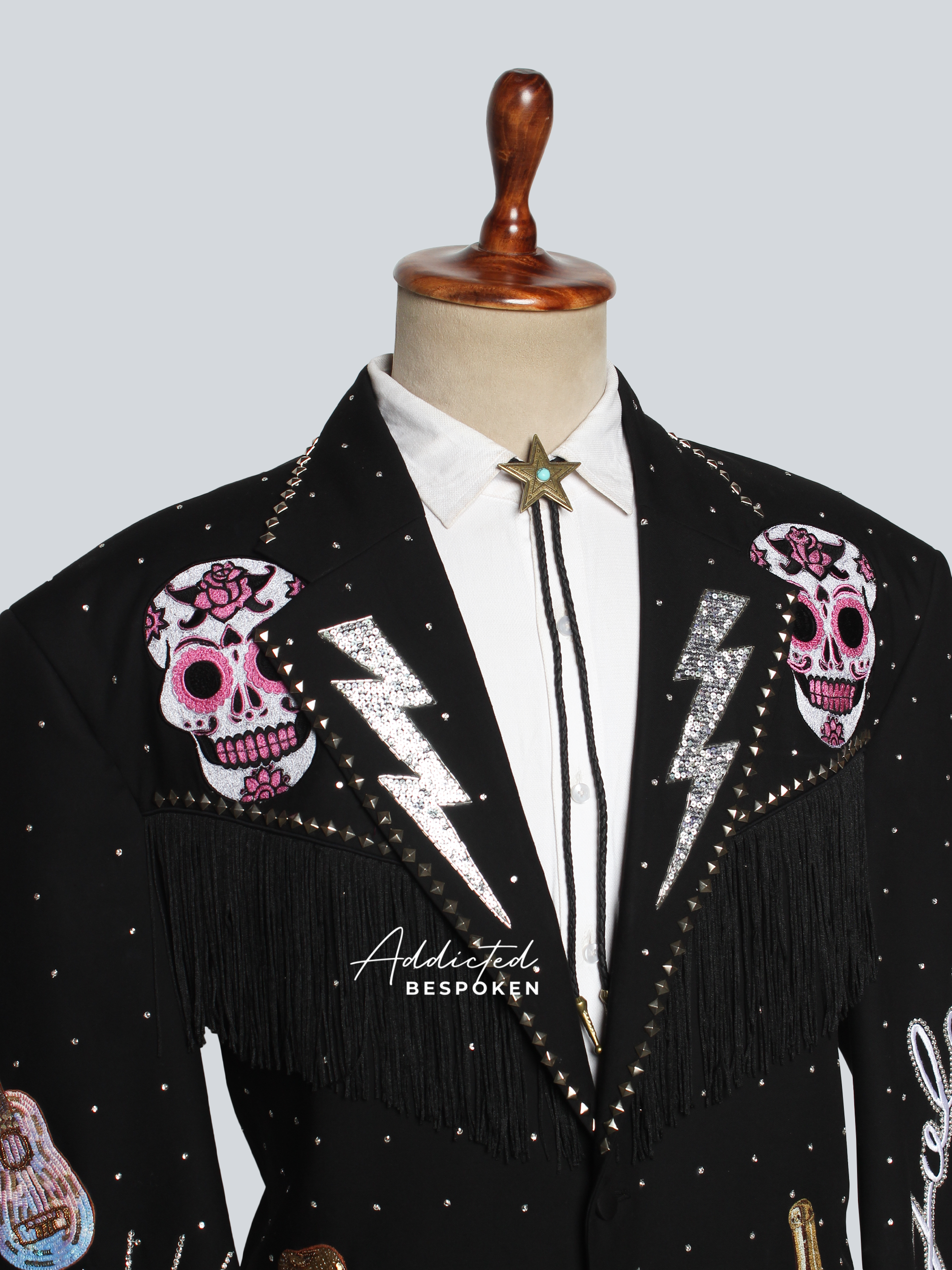 Black blazer with pink skull designs and fringe on a mannequin against a light gray background.