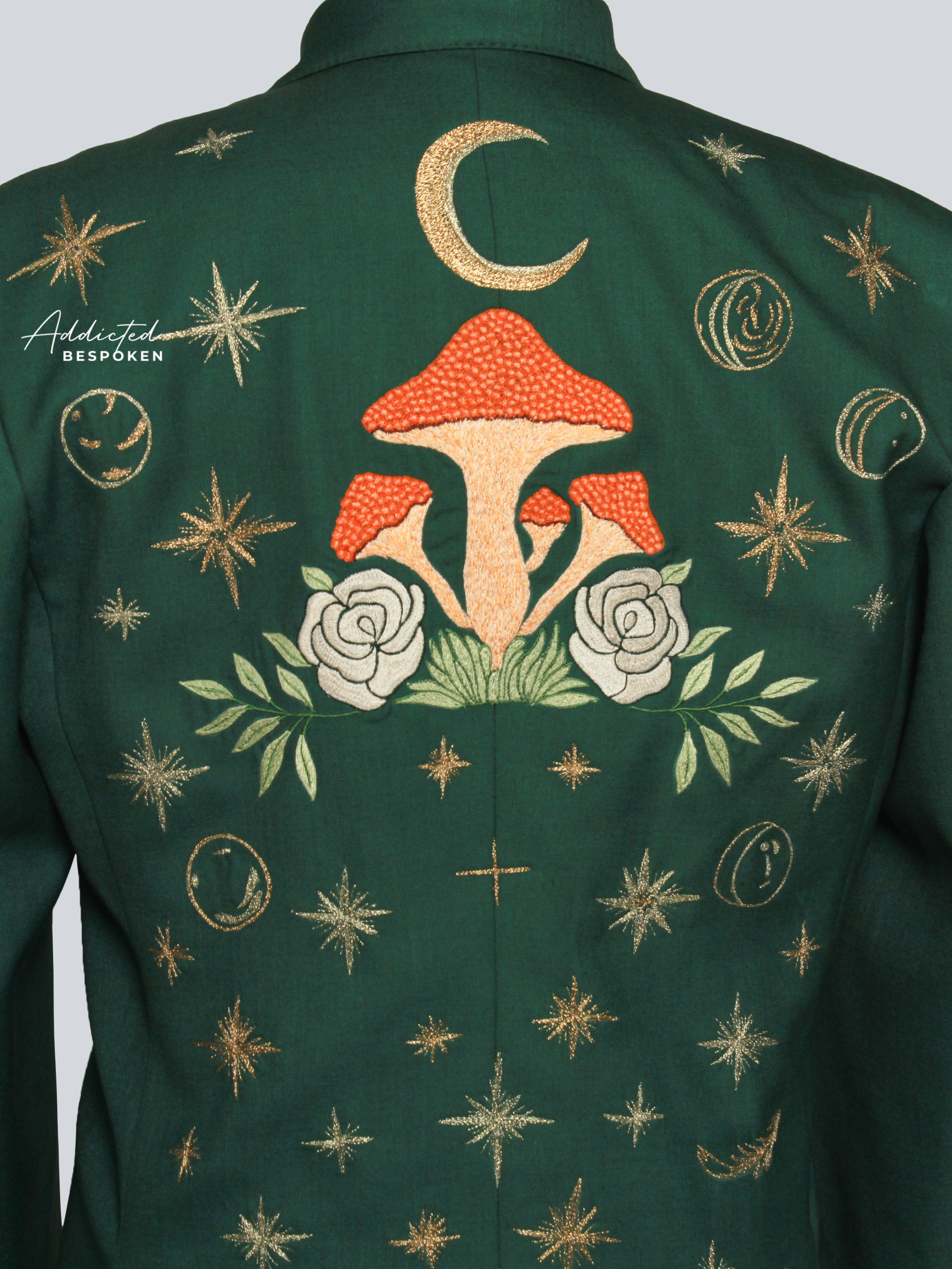 Green embroidered jacket with mushrooms, flowers, and celestial designs on a plain background