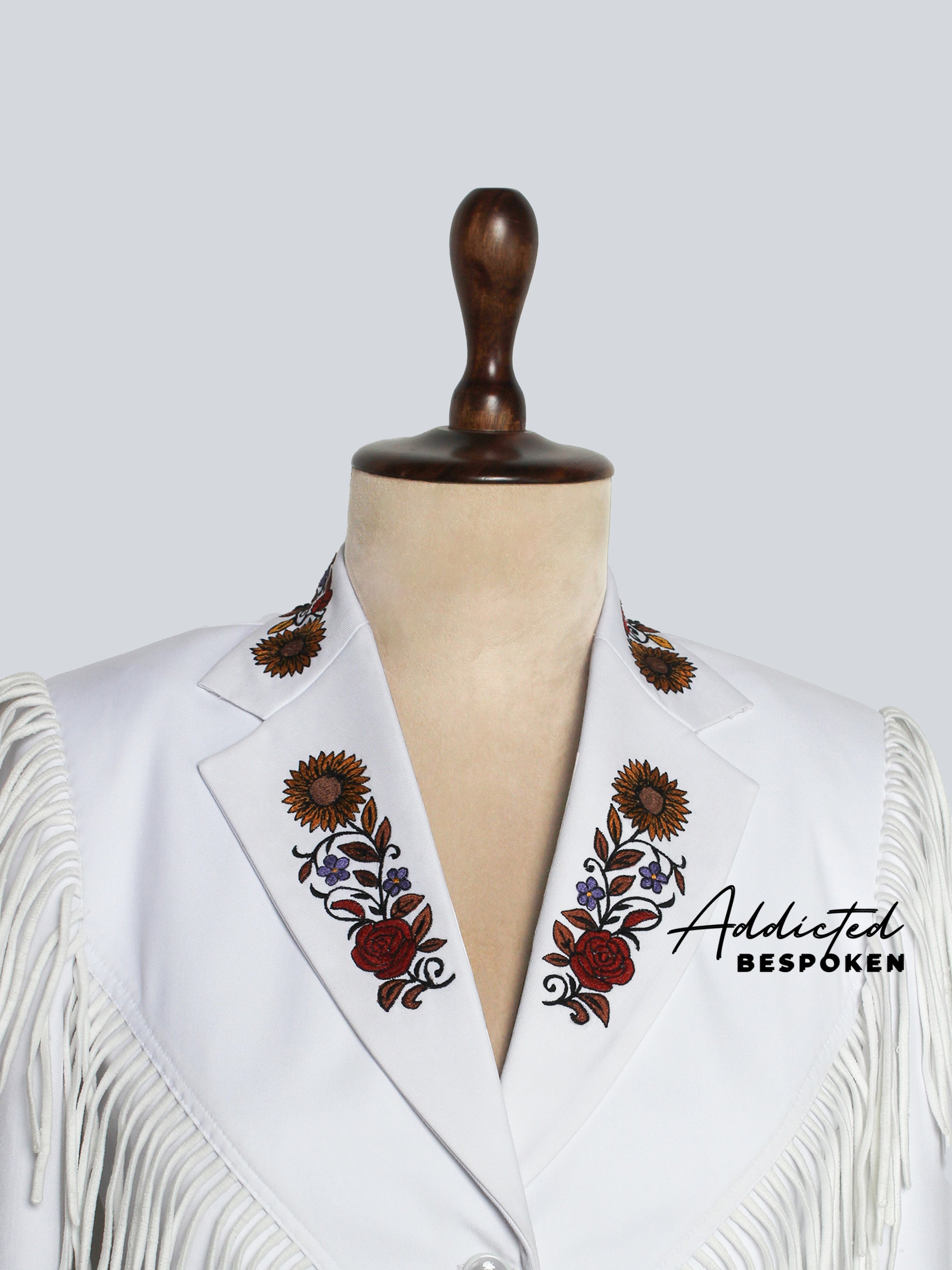 Close-up of a White jacket with floral embroidery and fringe on a mannequin against a white background, branded 'Addicted Bespöken'.