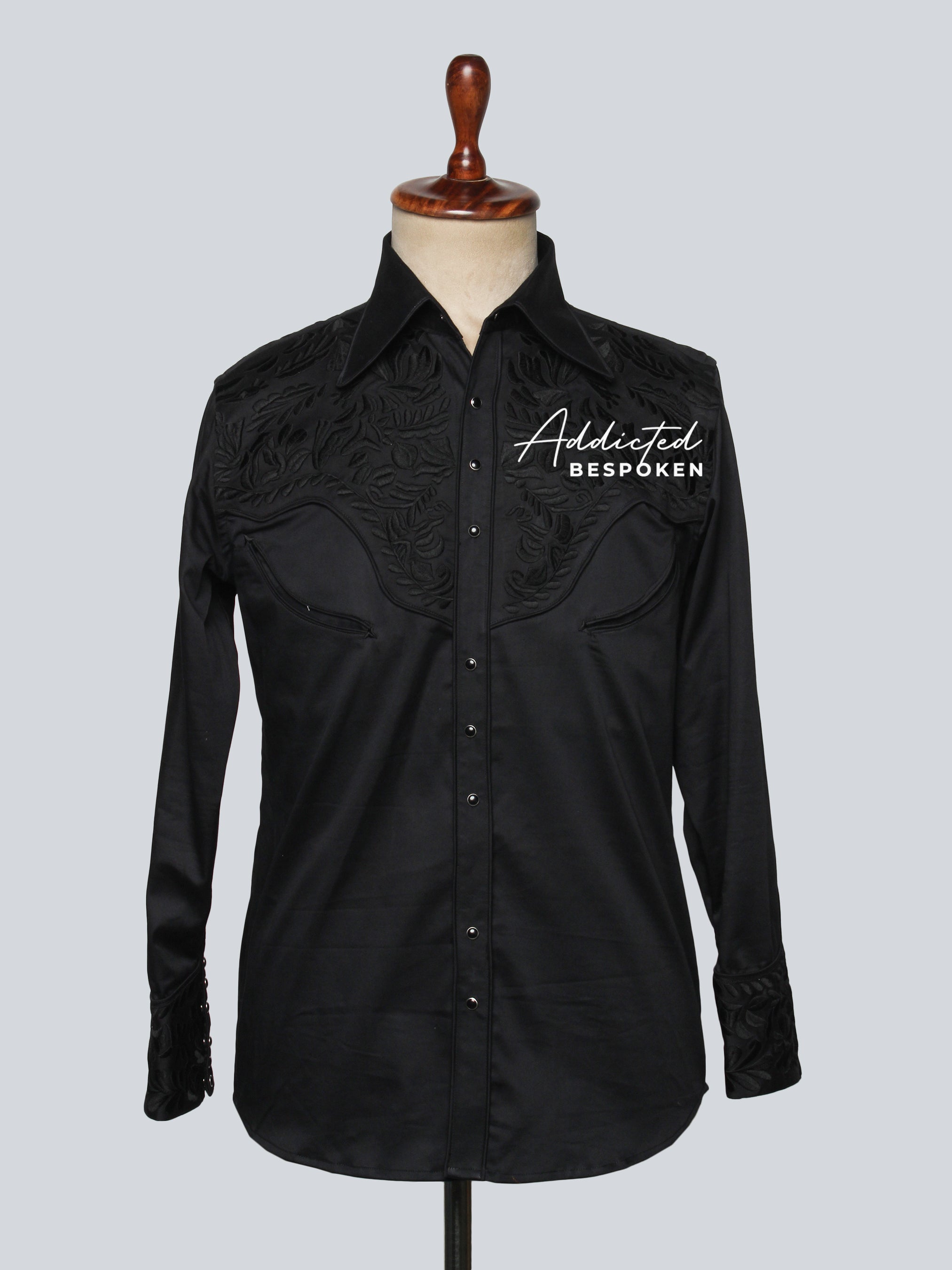 A black long-sleeved shirt with custom initial embroidery on the cuffs, displayed on a mannequin.