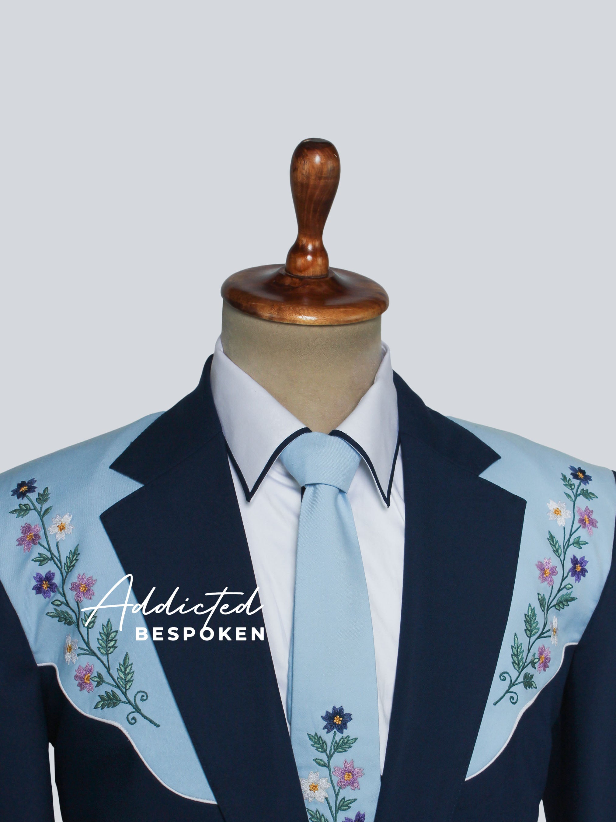 Mannequin wearing a navy blazer with floral embroidery and a light blue tie on a white background.