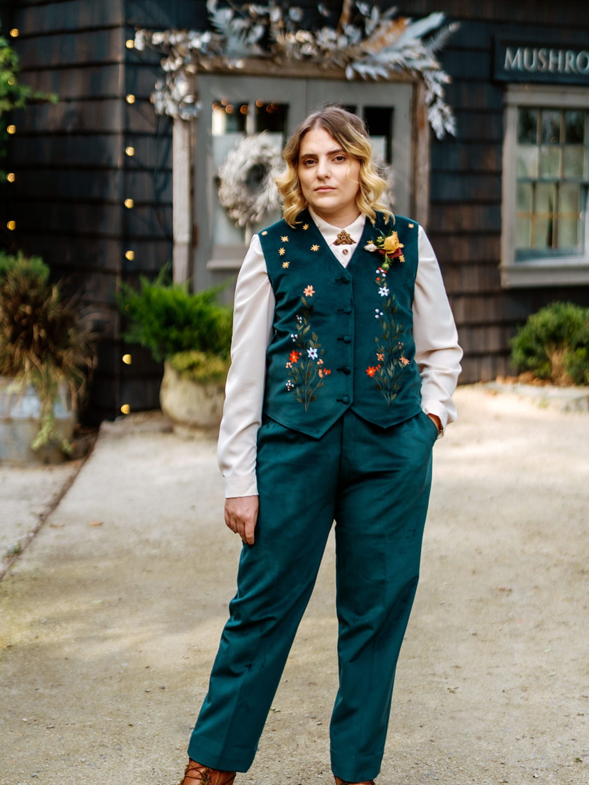 Person wearing a green suit with floral embroidery in front of a building with 'Mushroom' sign.