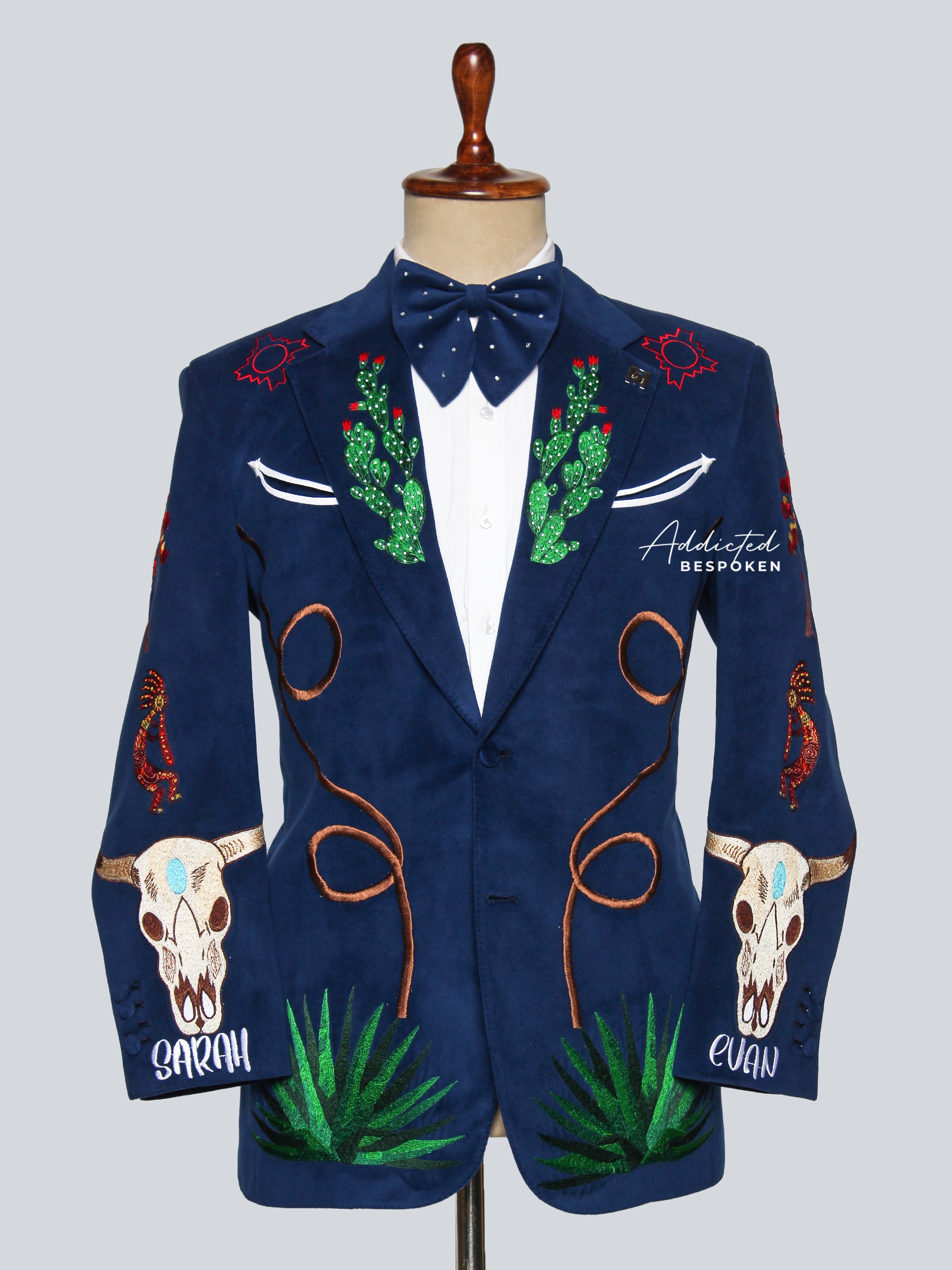 A navy blazer with desert-inspired embroidery, featuring motifs such as cactus blooms, coiled lassos, steer skulls, and agave plants, displayed on a mannequin.