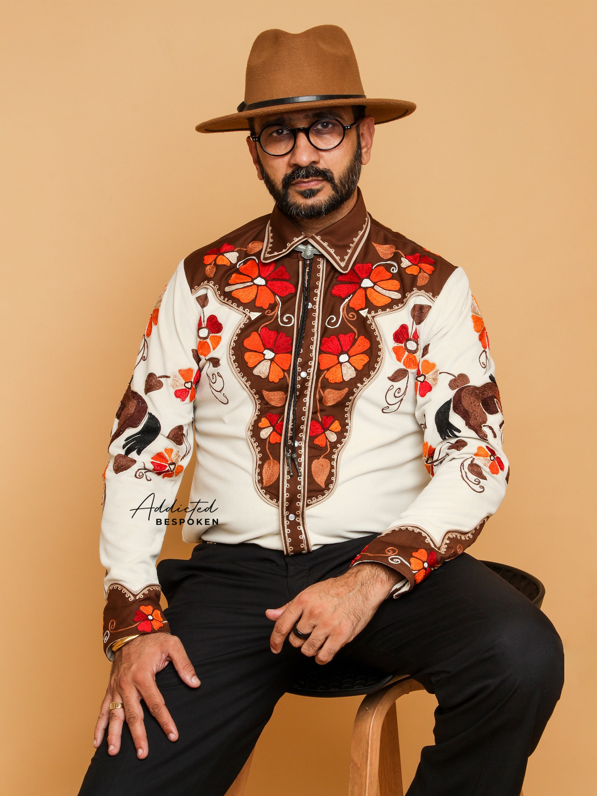 Seated front view of male model in cream embroidered western shirt with red floral details โ Addicted Bespoken