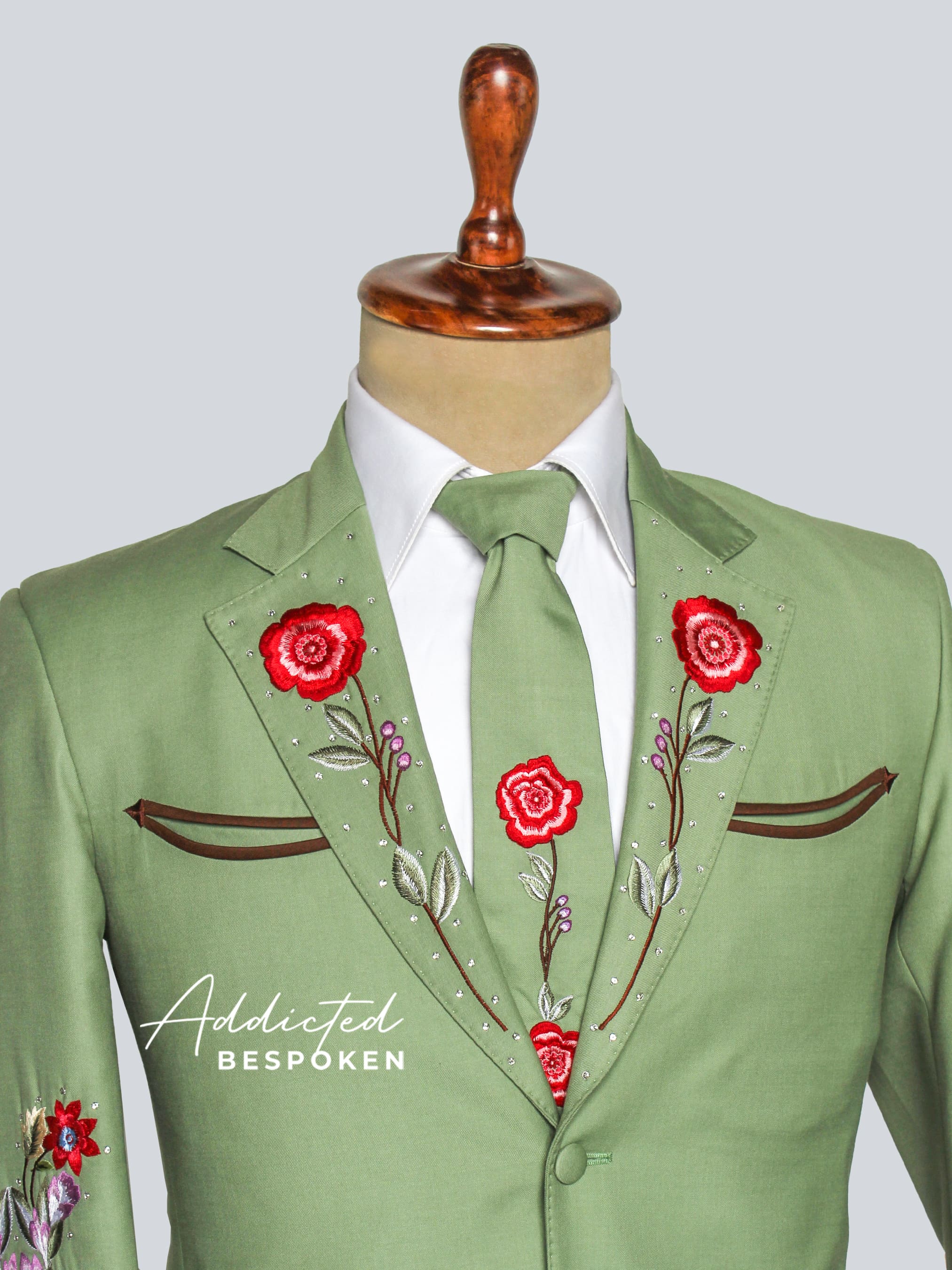 Green suit jacket with floral embroidery on a mannequin against a light gray background.