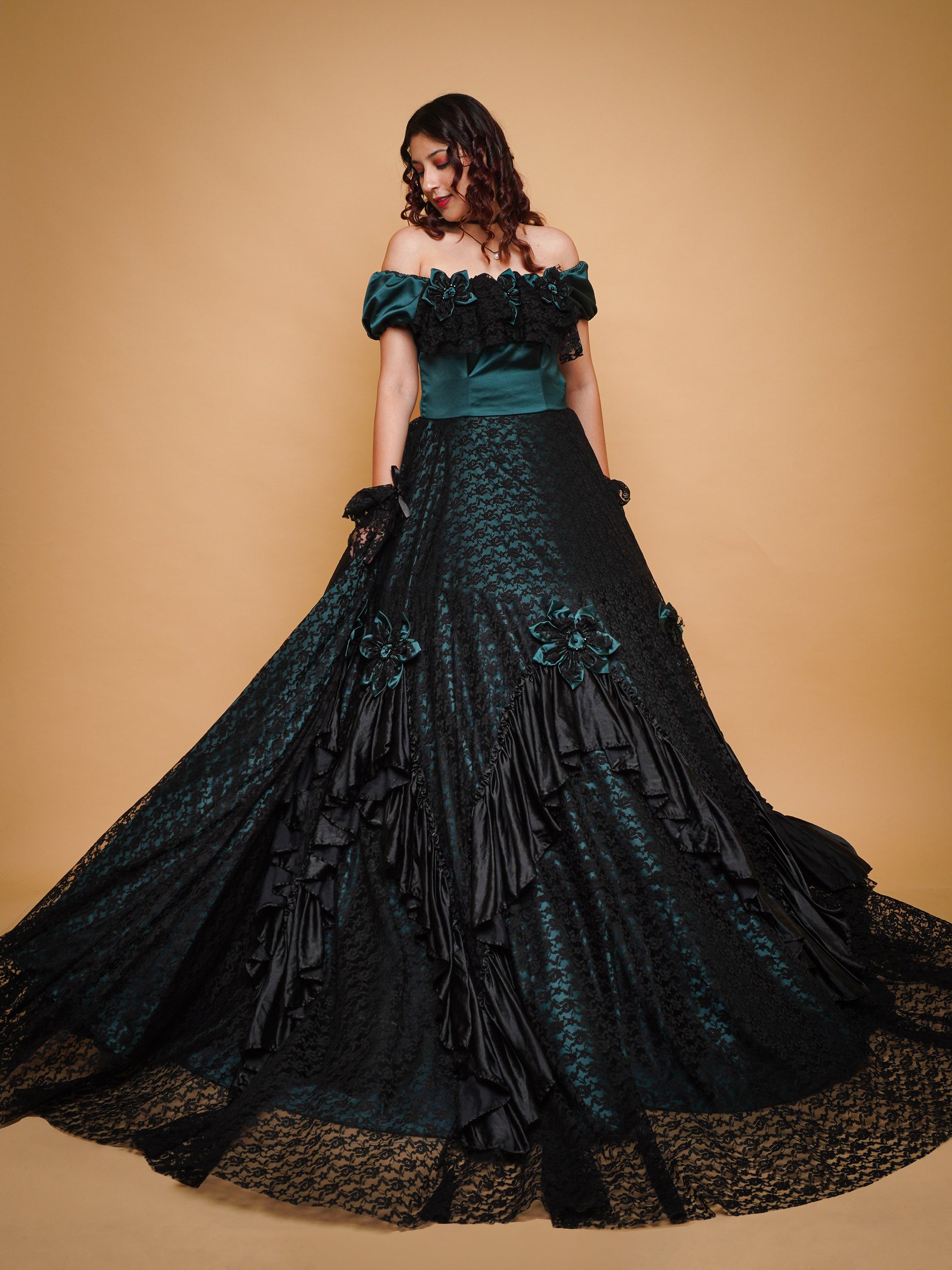 A woman modeling a Victorian-inspired gothic gown with green satin bodice and black lace netting, featuring intricate lace detailing and off-the-shoulder neckline.