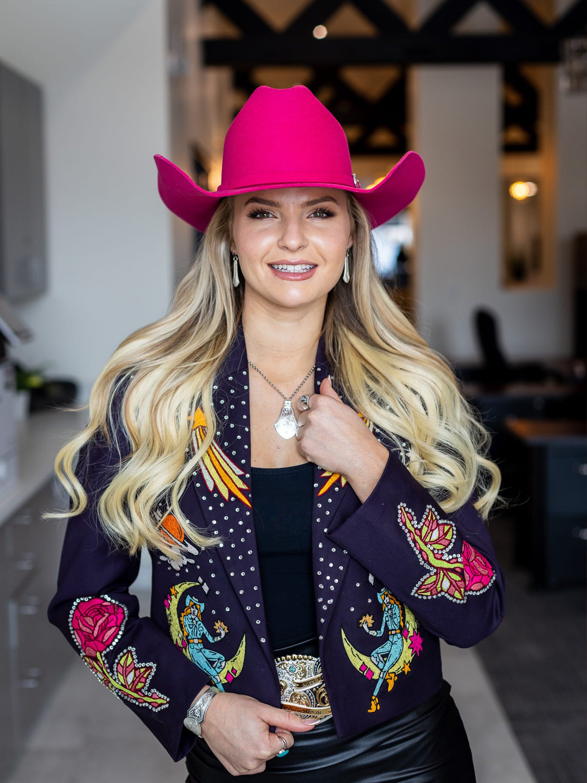 Woman wearing a bright pink cowboy hat and a dark bespoke blazer with colorful embroidered birds and floral motifs from Addicted Bespoken.