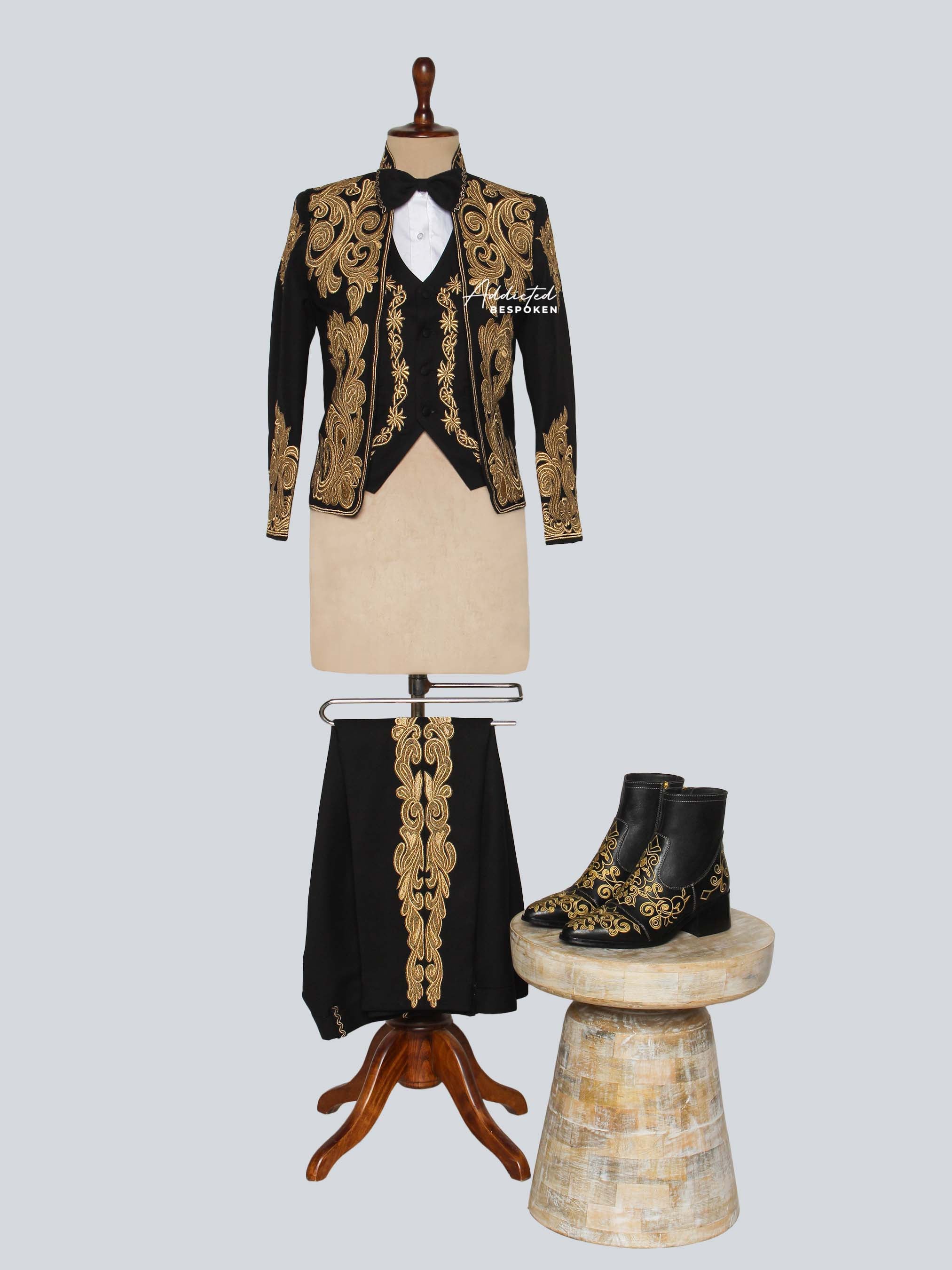 Black and gold embroidered formal outfit on a mannequin with boots on a light gray background