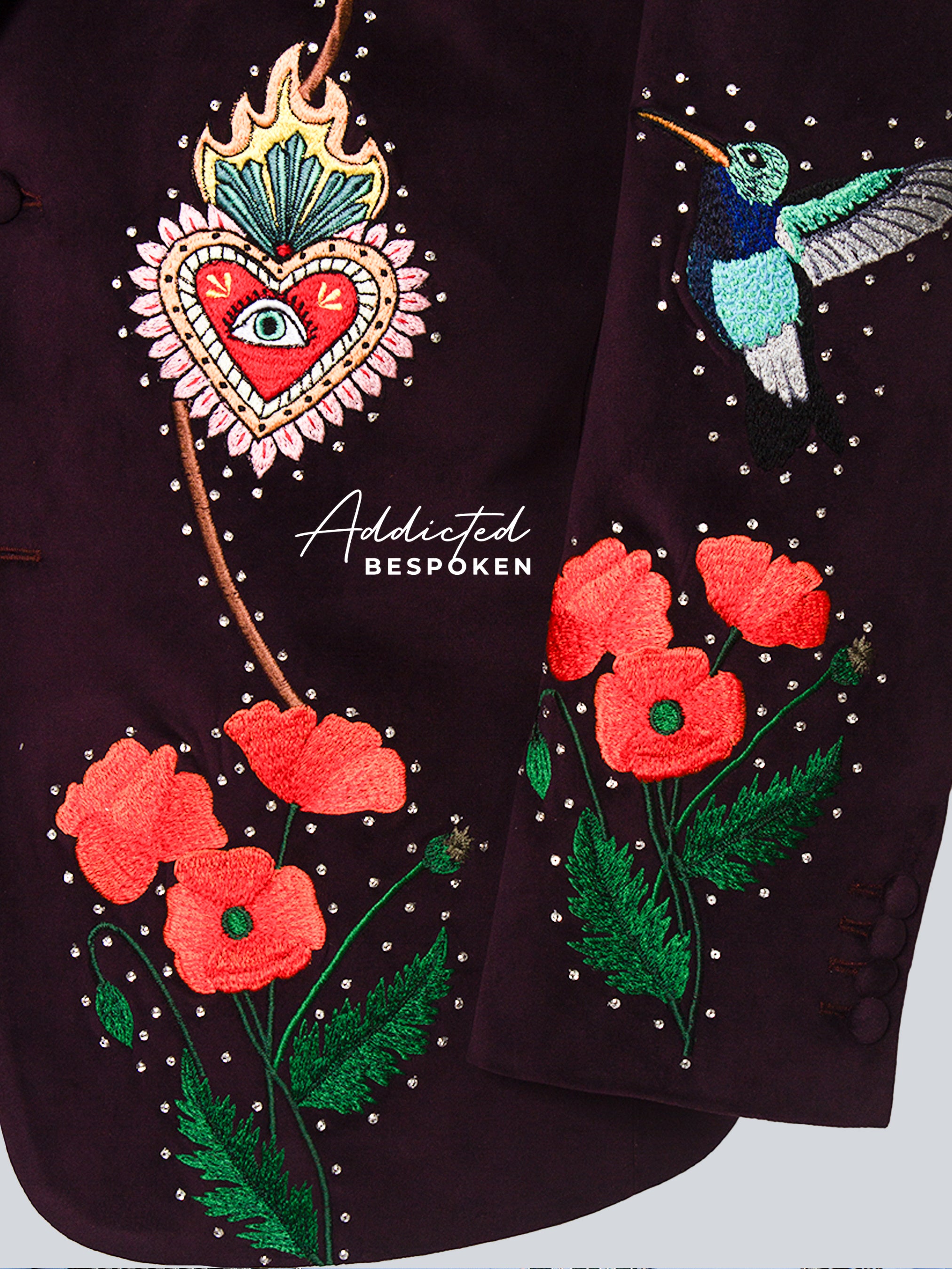 Embroidered details on a garment with flowers, a heart, and a hummingbird, featuring the brand 'Addicted Bespoke'.