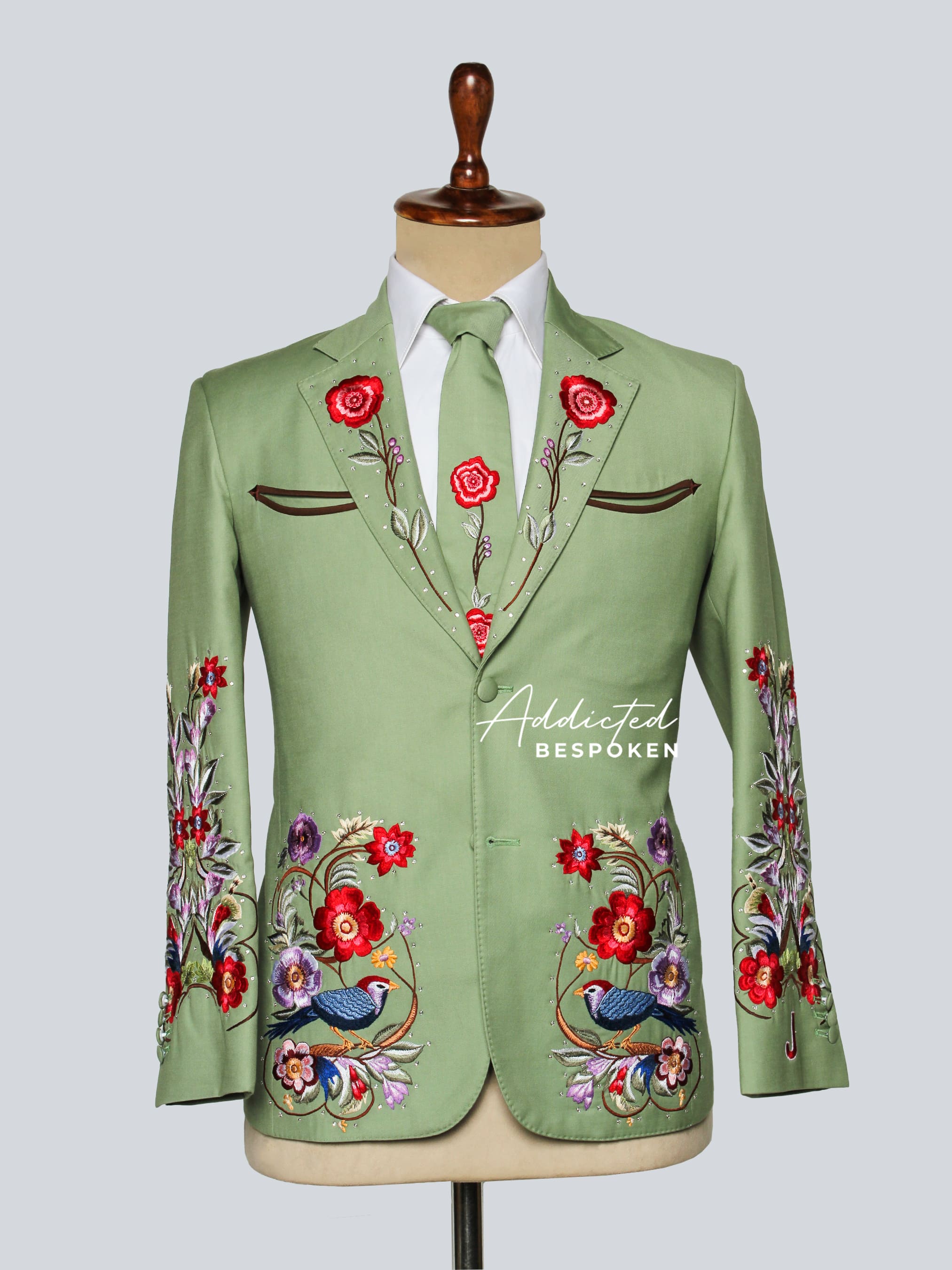 Green embroidered suit jacket on a mannequin with floral and bird designs.